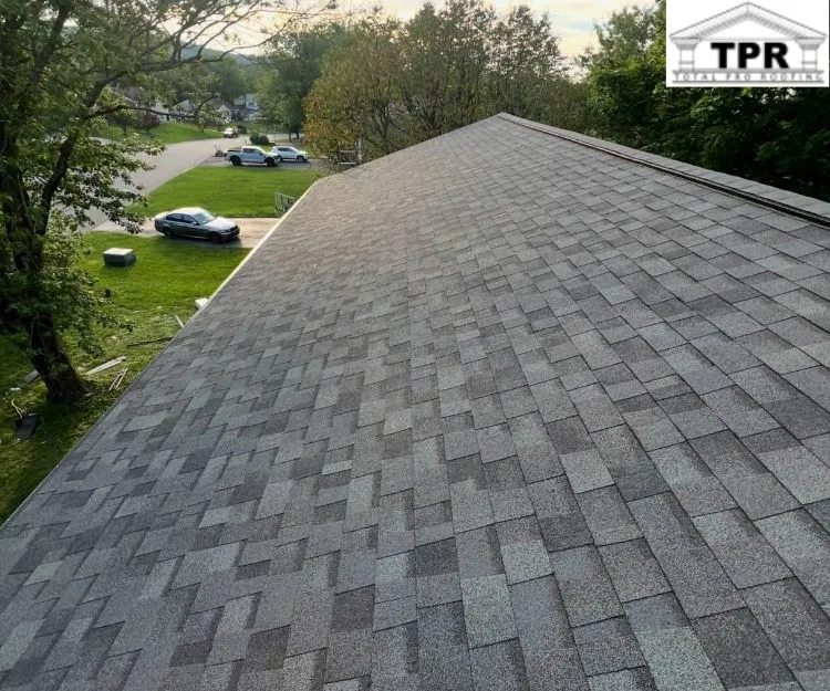 Overhead view of a completed gray asphalt shingle roof with trees and a neighborhood street visible in the background.